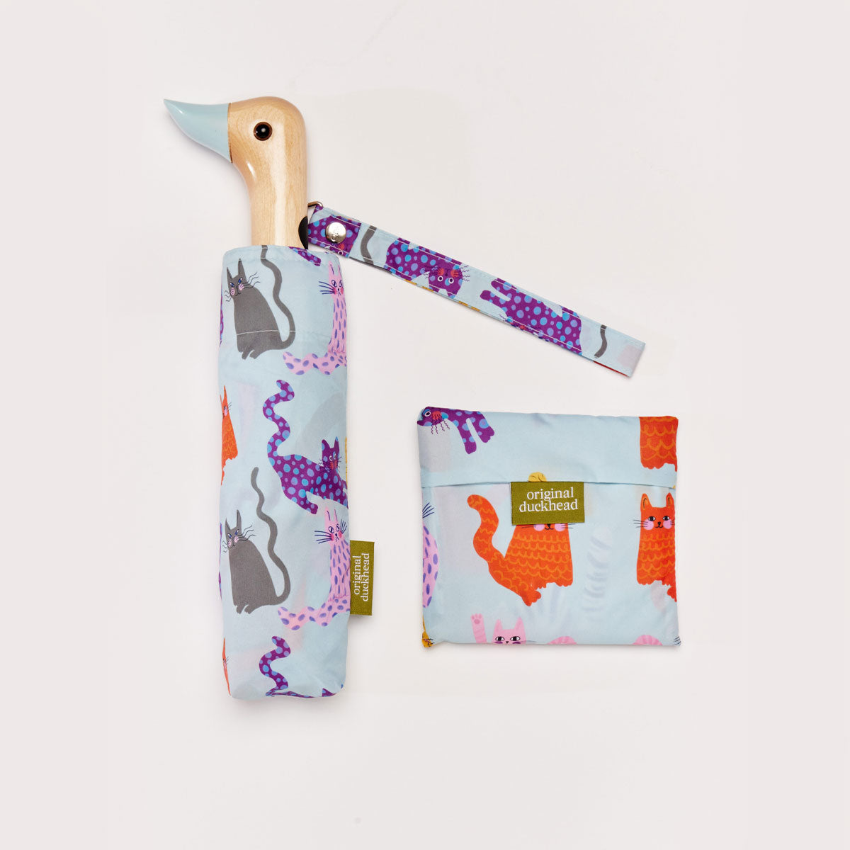 A blue umbrella with a duck head shaped handle next to a folded reusable tote bag on a plain white background
