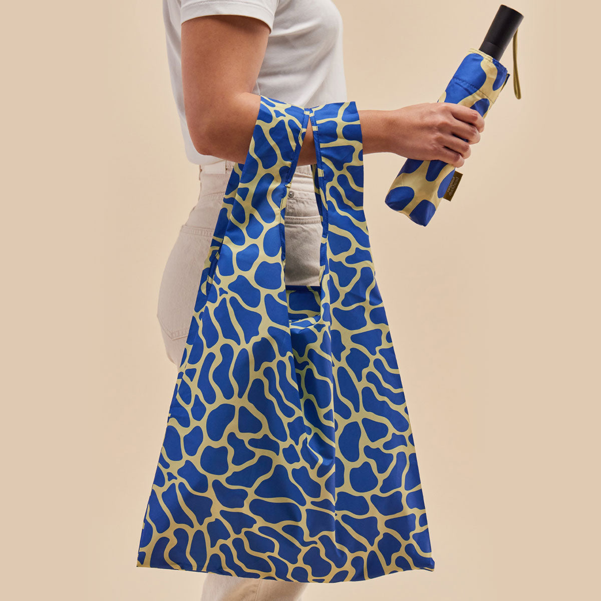 Person holding a blue and yellow patterned bag and umbrella against a beige background