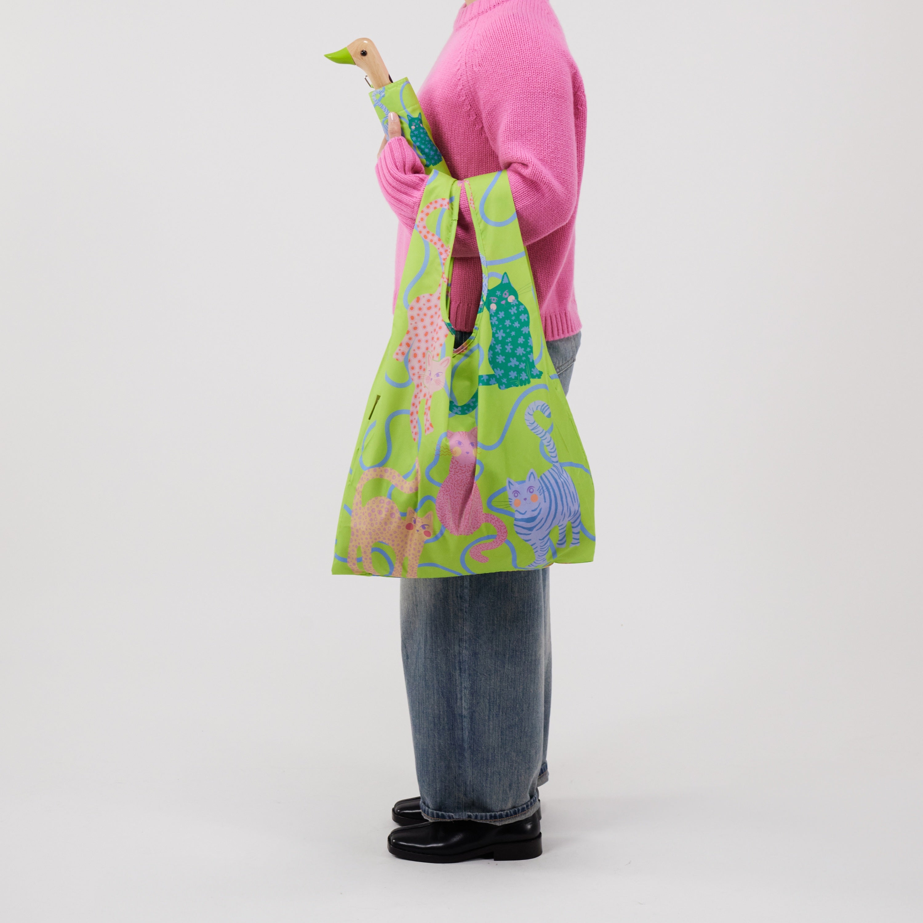 Person holding a colourful umbrella with duckhead handle and a matching tote bag with cat designs on a white background
