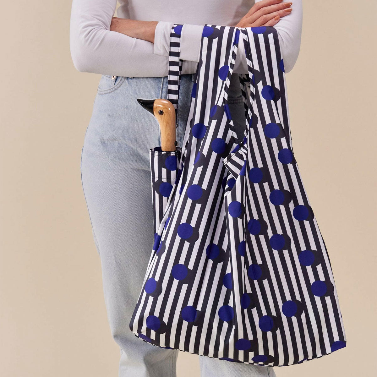 Person holding a striped umbrella with blue polka dots against a beige background
