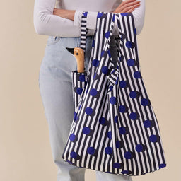 Person holding a striped umbrella with blue polka dots against a beige background