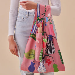 Person holding a colorful reusable bag with floral and vase prints on a beige background