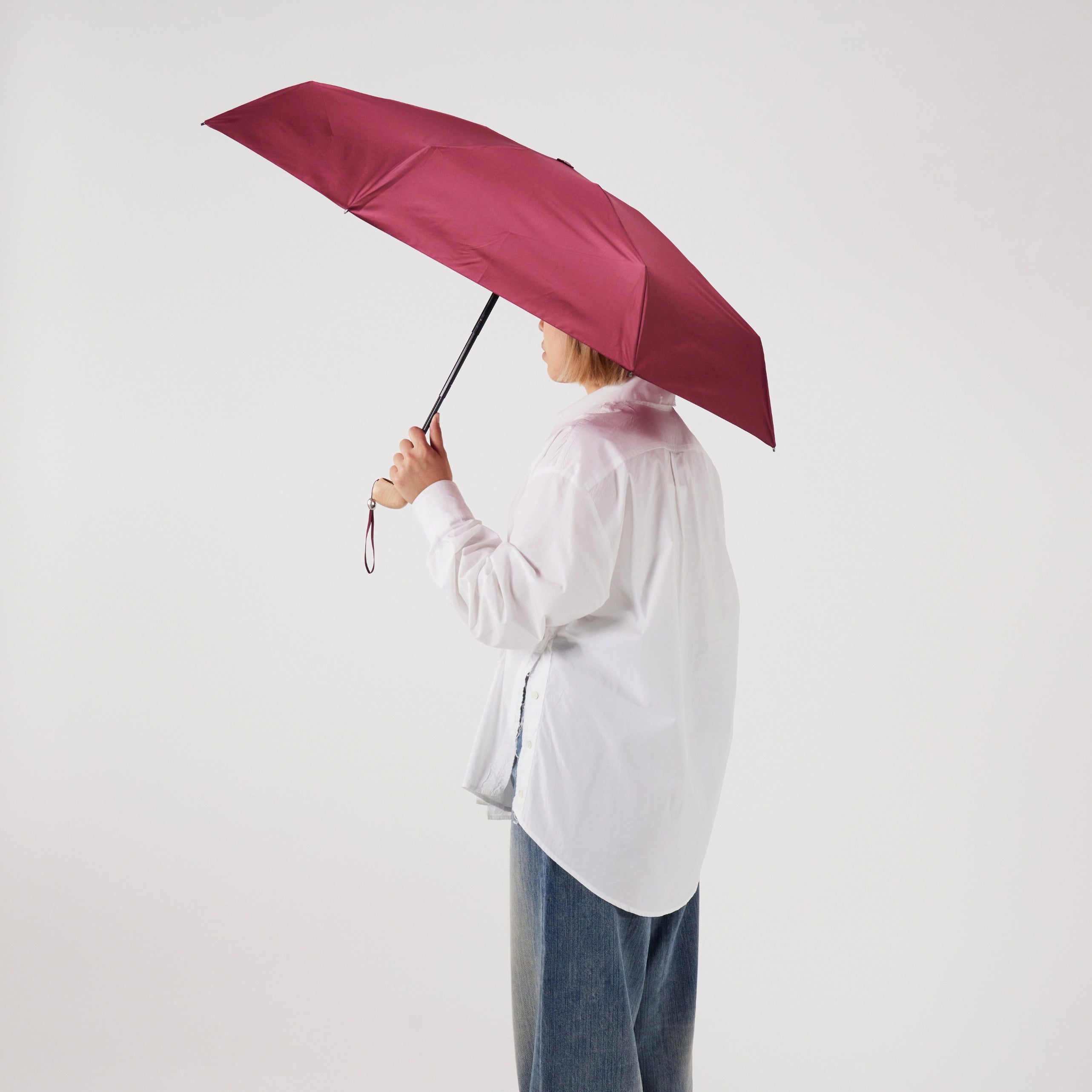 Person holding a cherry red umbrella against a white background