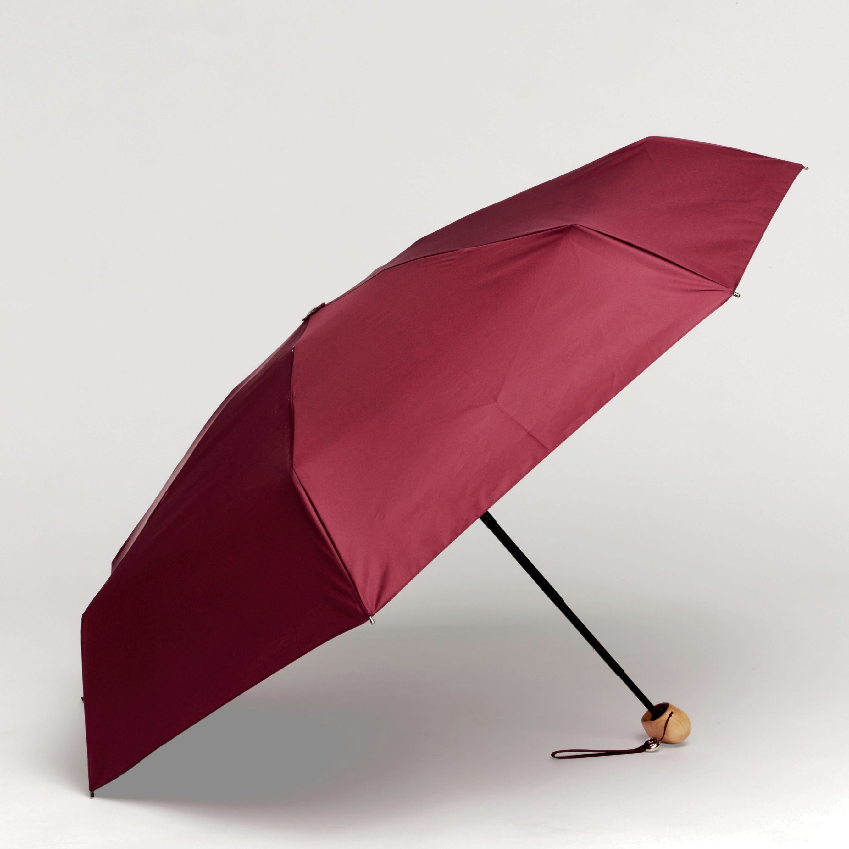 Cherry red umbrella with a wooden handle on a light gray background