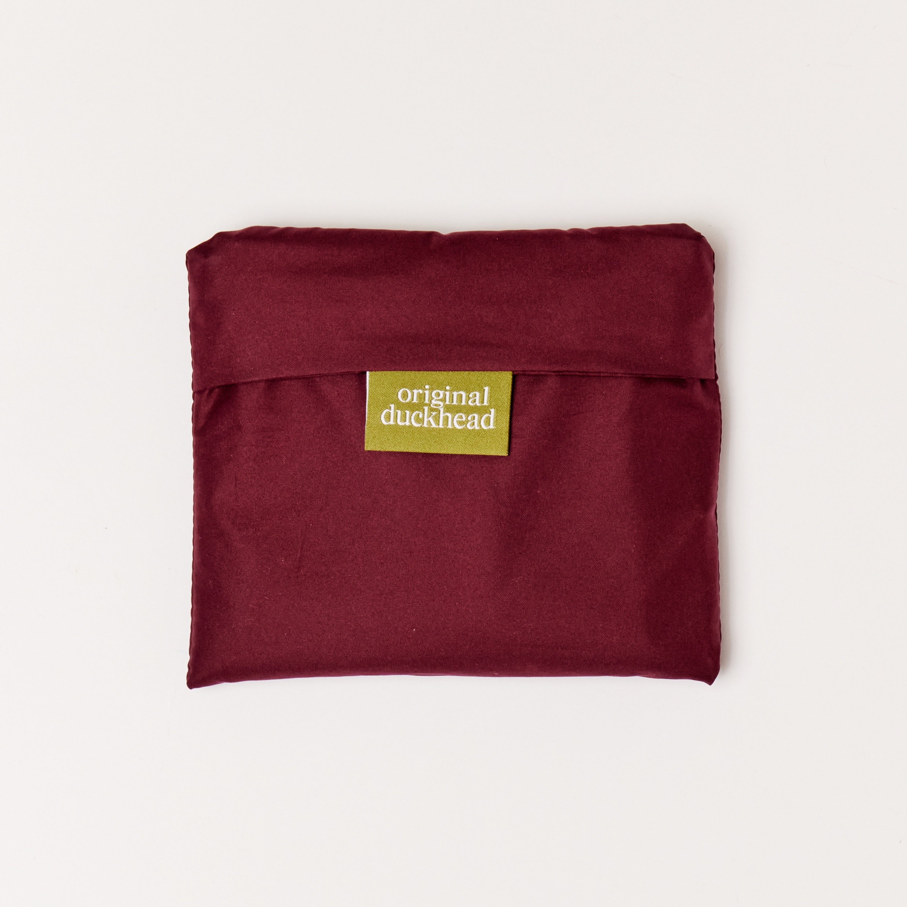 Folded cherry red reusable tote bag in pouch on a white background