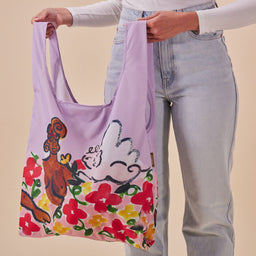 Person holding a colorful tote bag with characters and flowers against a beige background